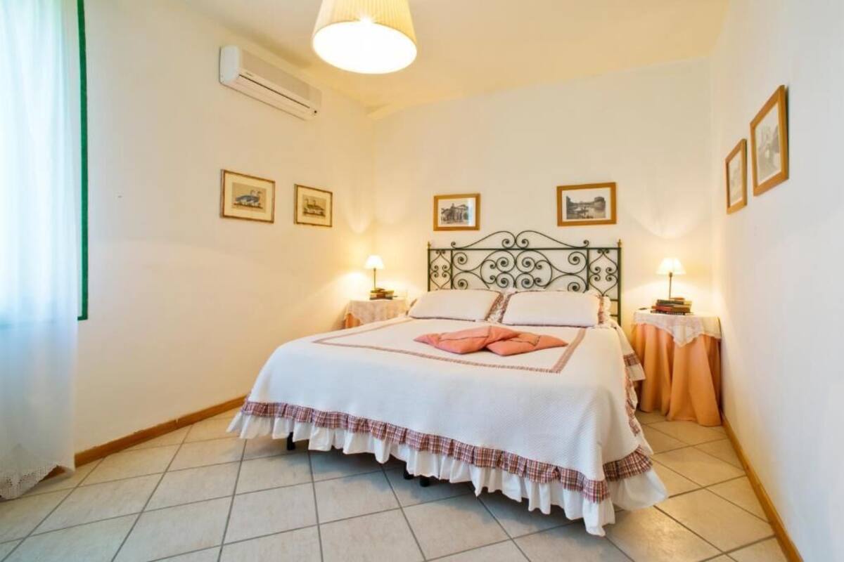 Una cama bien hecha con colcha blanca y roja a cuadros, dos lámparas de noche y cuadros en la pared.