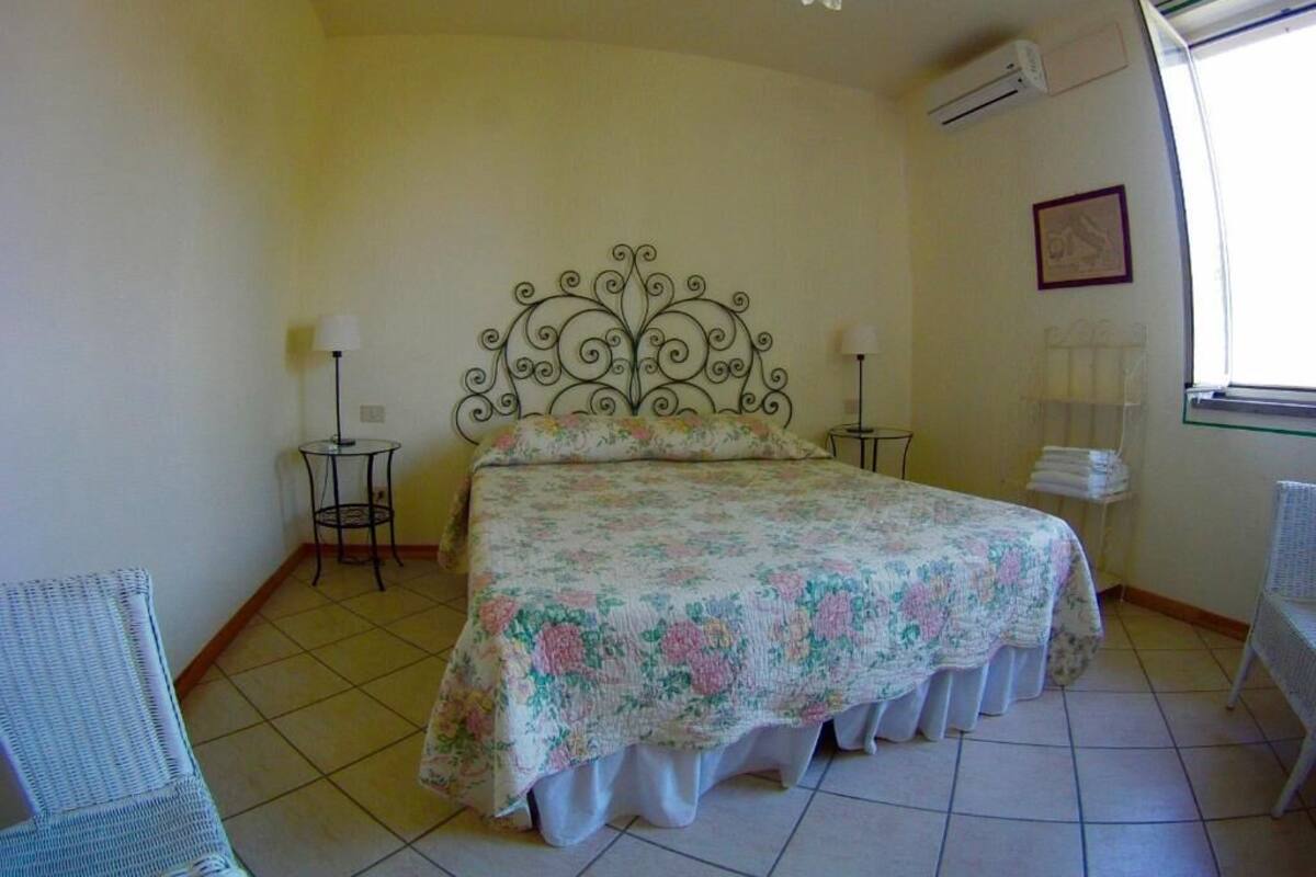 Un dormitorio con una cama, dos mesitas de noche, una silla y una ventana.