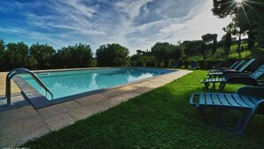 Una piscina amb una escala metàl·lica, envoltada d'herba i arbres.