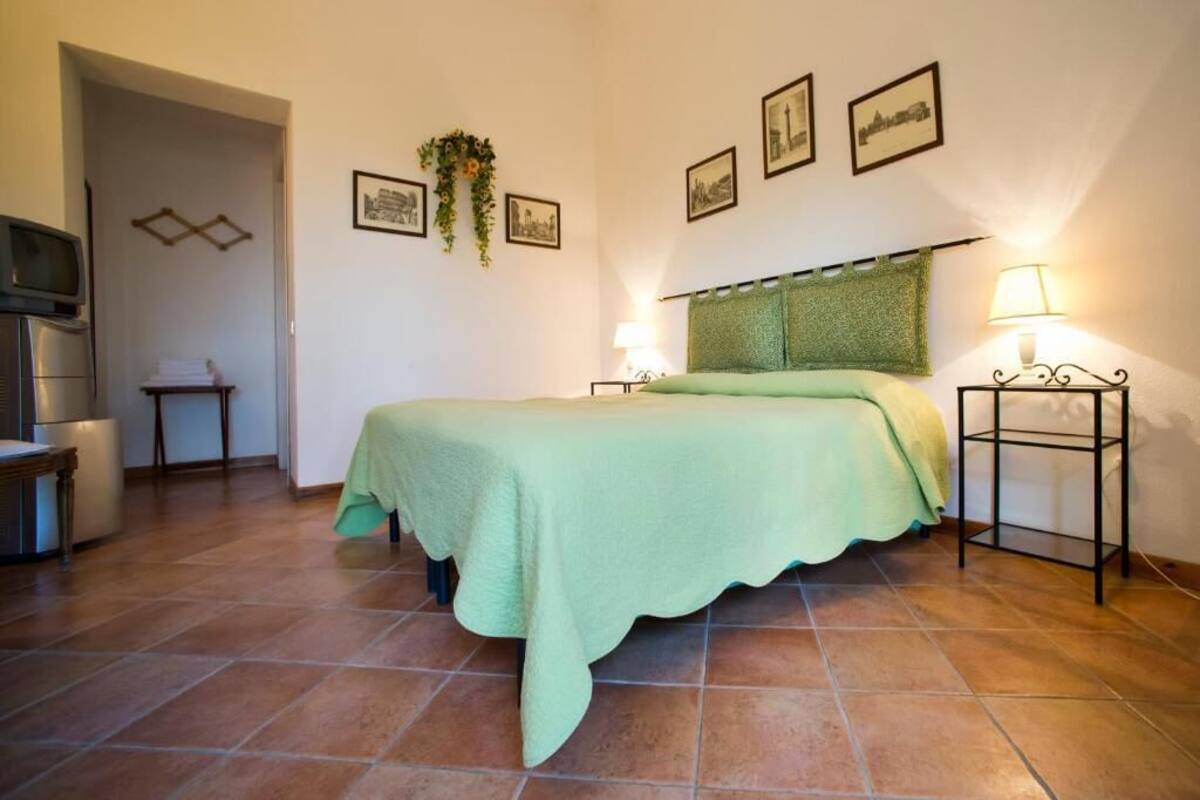 Un dormitorio con cama, televisor, una mesita y lámpara.