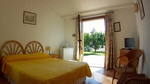 Habitació d'hotel amb un llit, una cadira, una televisió i una finestra amb cortines.