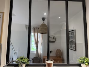 Een kamer met een groot raam, een rieten stoel, een klein tafeltje en een potplant.