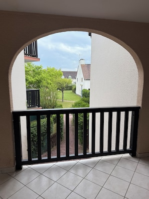 Een balkon met uitzicht op een tuin en een wit gebouw.