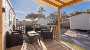 En overdækket terrasse med fletmøbler og et bord, med udsigt over en gade med mobilehomes.