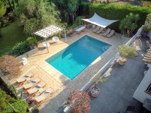 Ein rechteckiger Pool mit Liegestühlen und Sonnensegel, umgeben von Topfpflanzen und einem Garten.