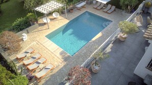 Et rektangulært swimmingpool med et hvidt markise, omgivet af liggestole og plantekrukker.