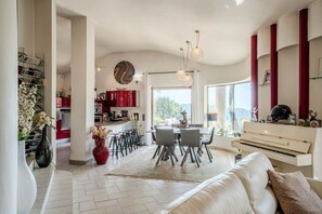 Ein geräumiger Wohnbereich mit einem weißen Sofa, einem Esstisch mit Stühlen, einer Küche mit roten Schränken und einem Klavier.
