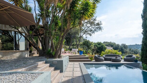A pool area with steps leading to a seating area, surrounded by tropical plants and overlooking a scenic landscape. - Magnifique villa avec piscine (Biot)