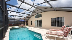 Una piscina con techo de cristal, un área de descanso con sillones y un edificio con amplios ventanales.