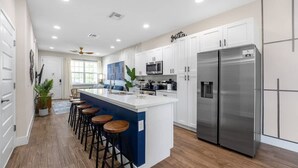 A modern kitchen with white cabinets, a stainless steel refrigerator, and a bar area with stools. - Renovated 4BR Townhome w/ Disney Game Room (Kissimmee)