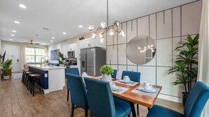 A modern kitchen with a central island, bar stools, and a dining area with blue chairs and a wooden table. - Renovated 4BR Townhome w/ Disney Game Room (Kissimmee)