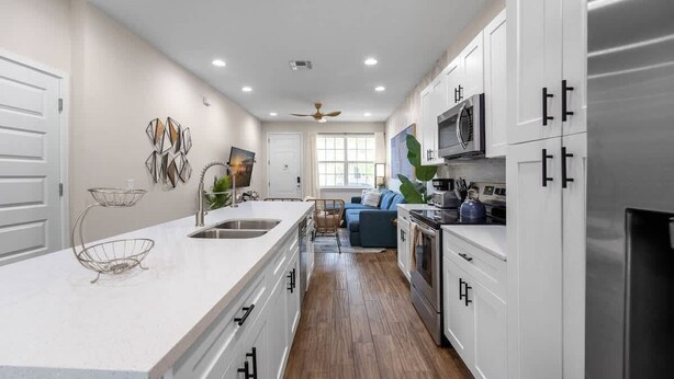 A modern kitchen with white cabinetry, a large island with a sink, and a dining area with a blue sofa. - Renovated 4BR Townhome w/ Disney Game Room (Kissimmee)
