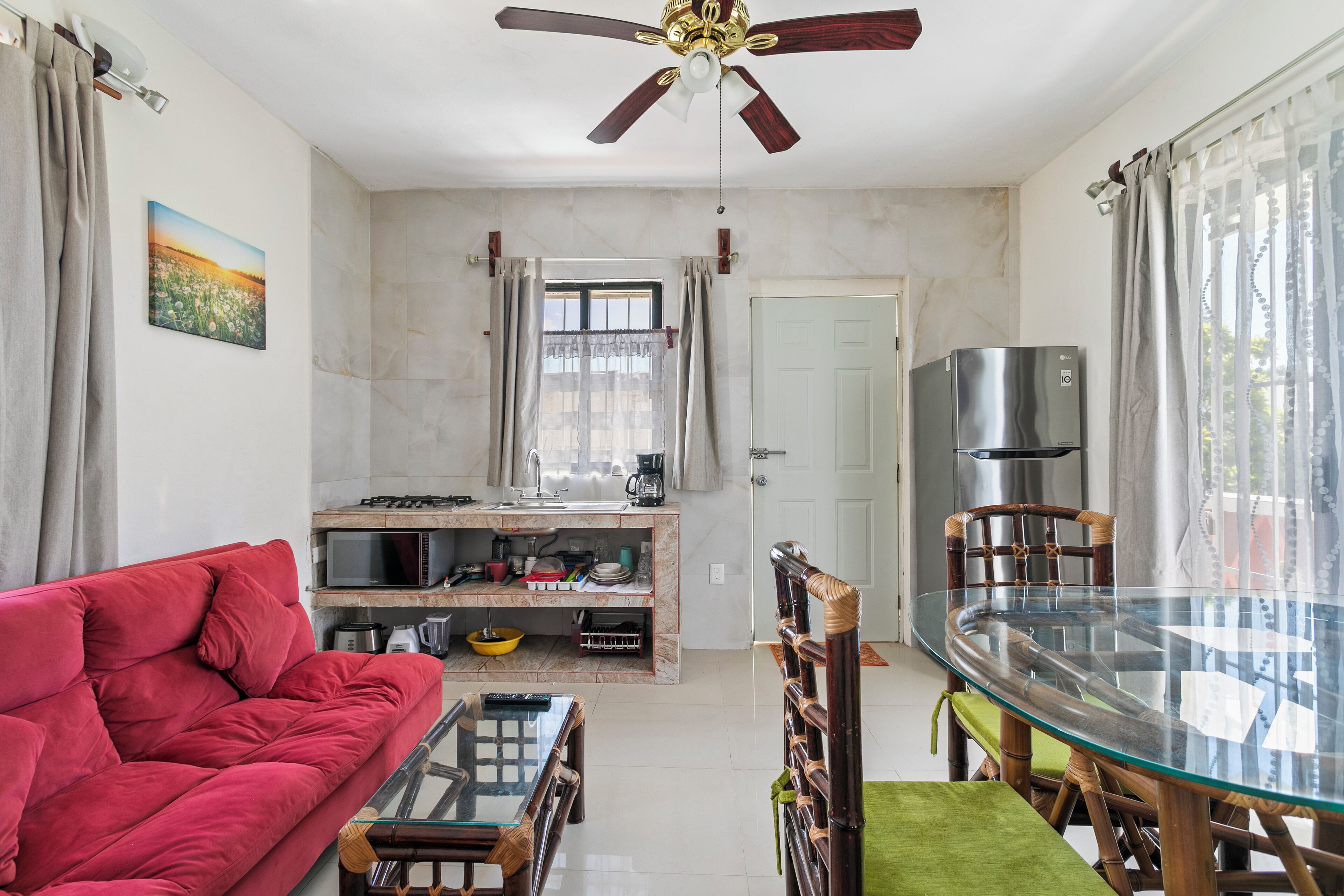 A compact living space with a sofa, a glass dining table, a kitchen area, and a ceiling fan.