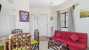 Ein Wohnzimmer mit einem roten Sofa, einem Glastisch und einem Bambusstuhl mit einem grünen Kissen.