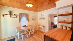 A cozy kitchen with wooden flooring, a dining table with chairs, a small desk, and shelves with kitchenware. - Lakeview, pet friendly apartment with lake access (Greenville)