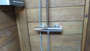 A wooden shower stall with a chrome showerhead and hose.