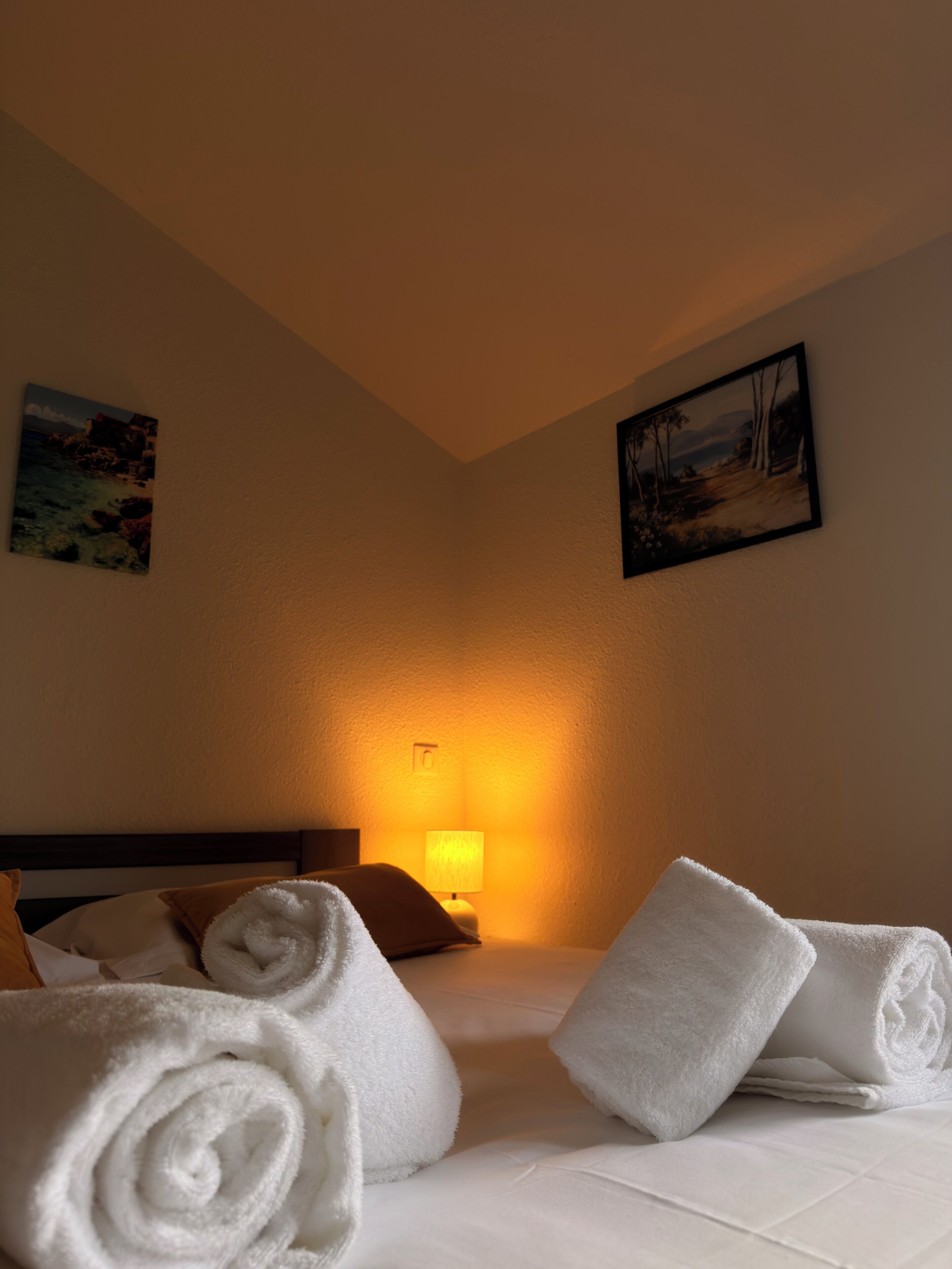 Habitación de hotel con una cama bien hecha, una lámpara y dos cuadros en las paredes.