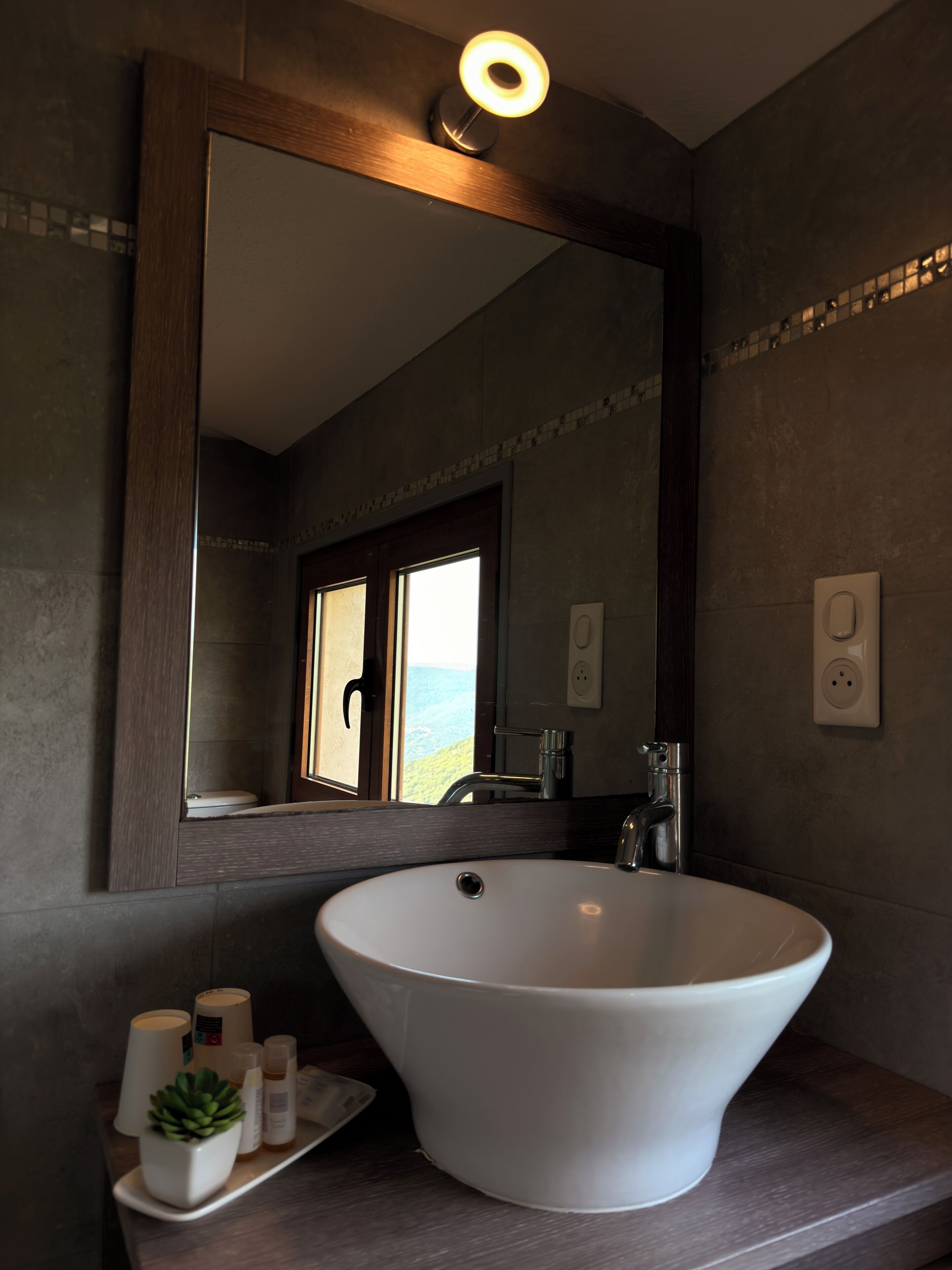 Un baño con un lavamanos grande de color blanco, un espejo y una ventana con vistas.