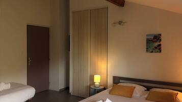 Quarto de hotel com uma cama, mesa de cabeceira com abajur, porta e um quadro na parede.