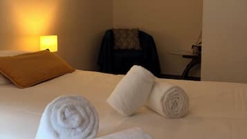 Habitación de hotel con cama, dos toallas enrolladas, una silla, un escritorio, una lámpara y un cuadro en la pared.
