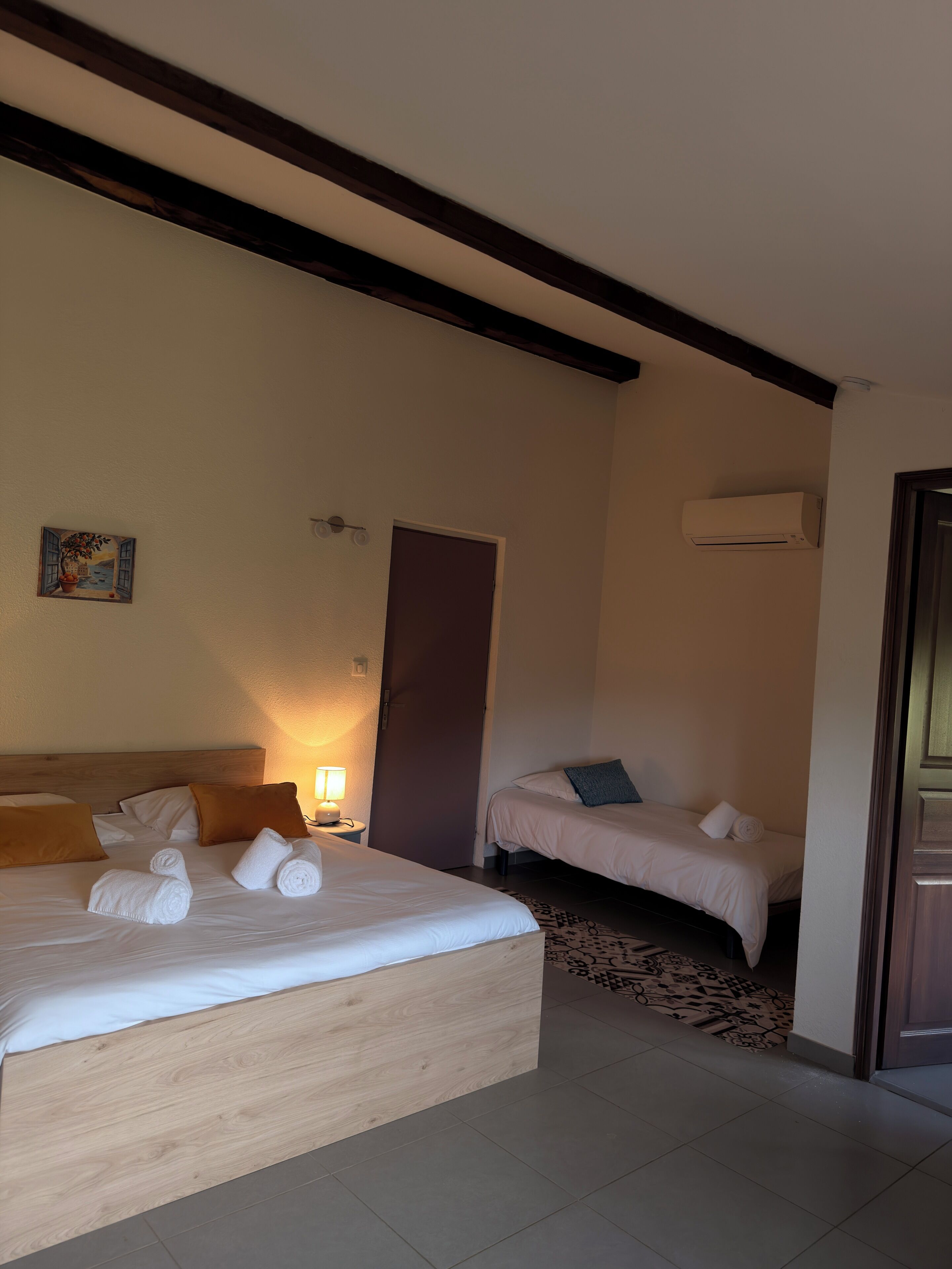Habitación de hotel con una cama grande, una cama más pequeña, una puerta, un equipo de aire acondicionado y un cuadro colgado en la pared.