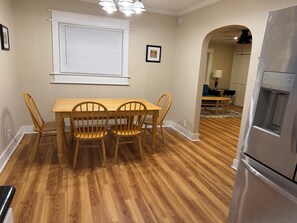 A dining area with a wooden table and chairs, a window with blinds, a refrigerator, and a hallway leading to another room. - Enjoyable 2-bedroom house in Tukwila perfect for your getaway (Tukwila)