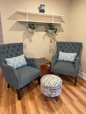 A room with two grey upholstered armchairs with patterned cushions, a small wooden side table, and a matching ottoman. There are two potted plants on white shelves above the table. - Enjoyable 2-bedroom house in Tukwila perfect for your getaway (Tukwila)