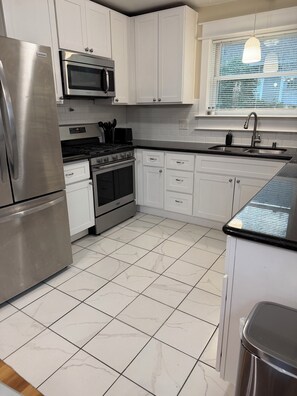 A modern kitchen with white cabinets, stainless steel appliances, and a tiled floor. - Enjoyable 2-bedroom house in Tukwila perfect for your getaway (Tukwila)