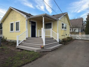 A yellow single-story house with a front porch, a black door, and a white picket fence. - Enjoyable 2-bedroom house in Tukwila perfect for your getaway (Tukwila)