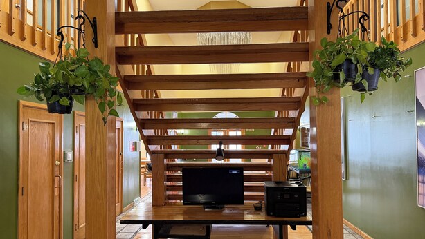 Une structure de pergola en bois, avec un téléviseur à écran plat et une imprimante posés sur une table, le tout entouré de murs verdoyants et de planchers en bois.