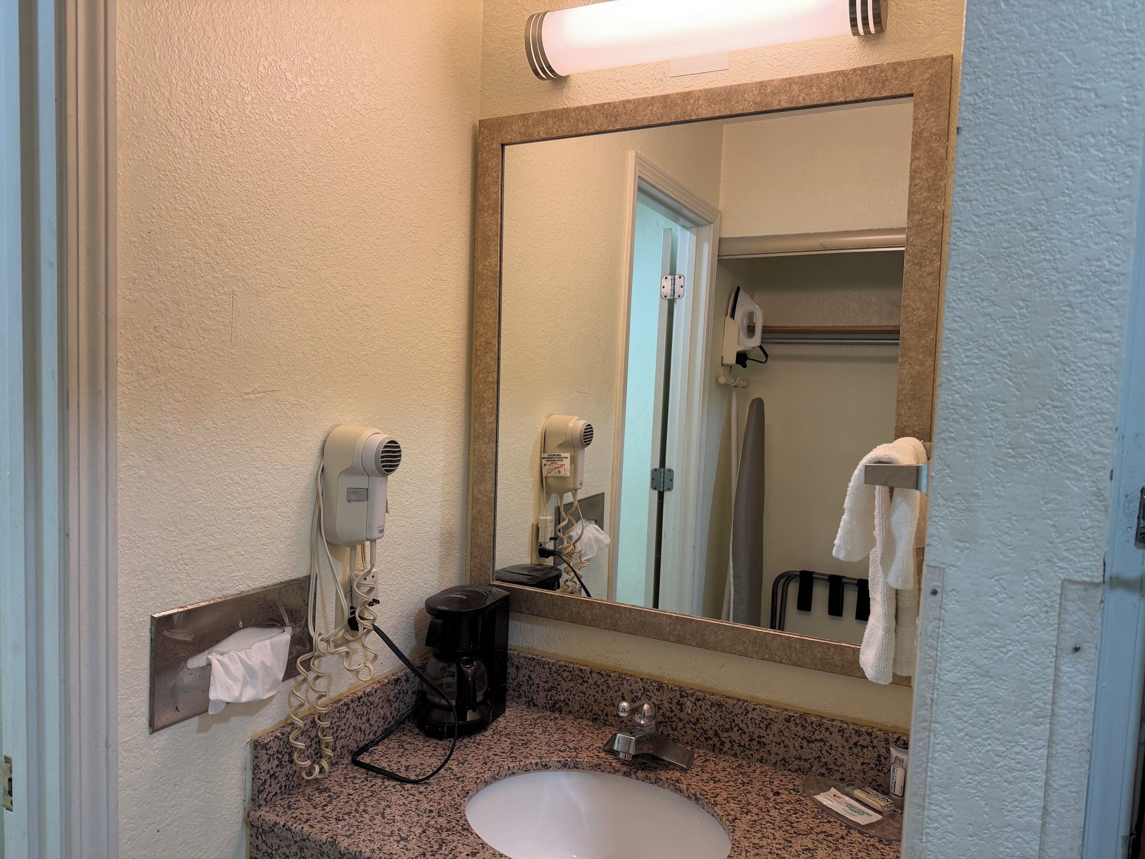A bathroom with a sink, a mirror, a hairdryer, and an ironing board.
