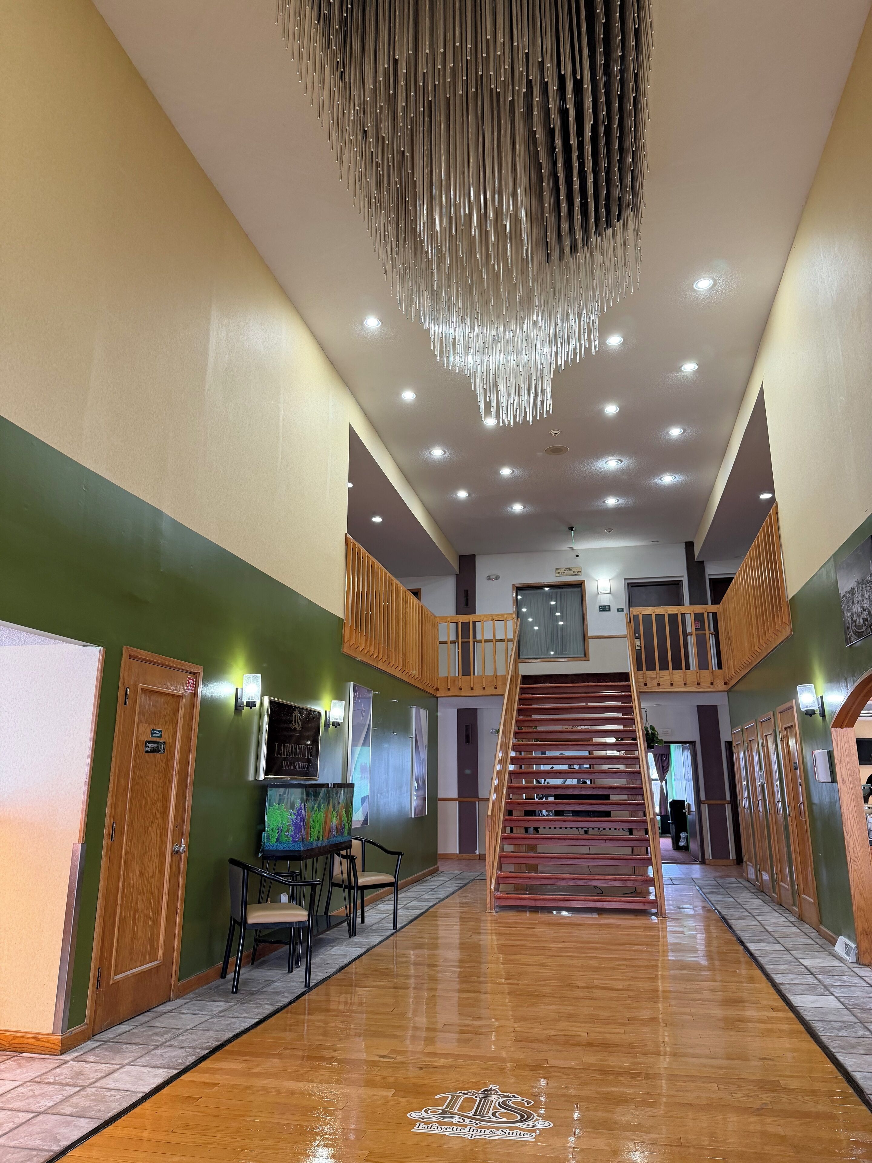 A spacious lobby with a wooden staircase, a chandelier, and a sign for 'Lafayette Jim Suites'.