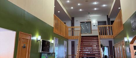 A spacious lobby with a wooden staircase, a chandelier, and a sign for 'Lafayette Jim Suites'.