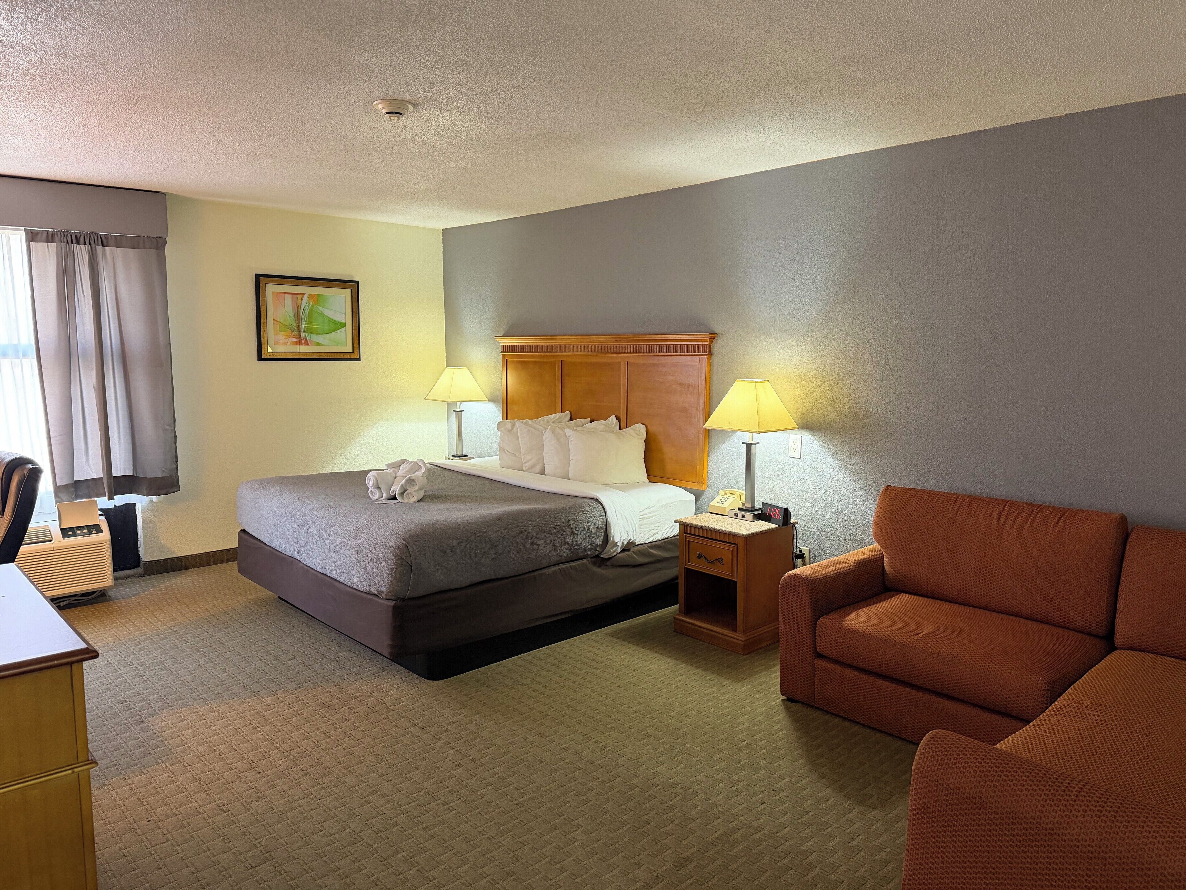 A hotel room with a bed, two bedside lamps, a wooden nightstand, a chair, and a desk.