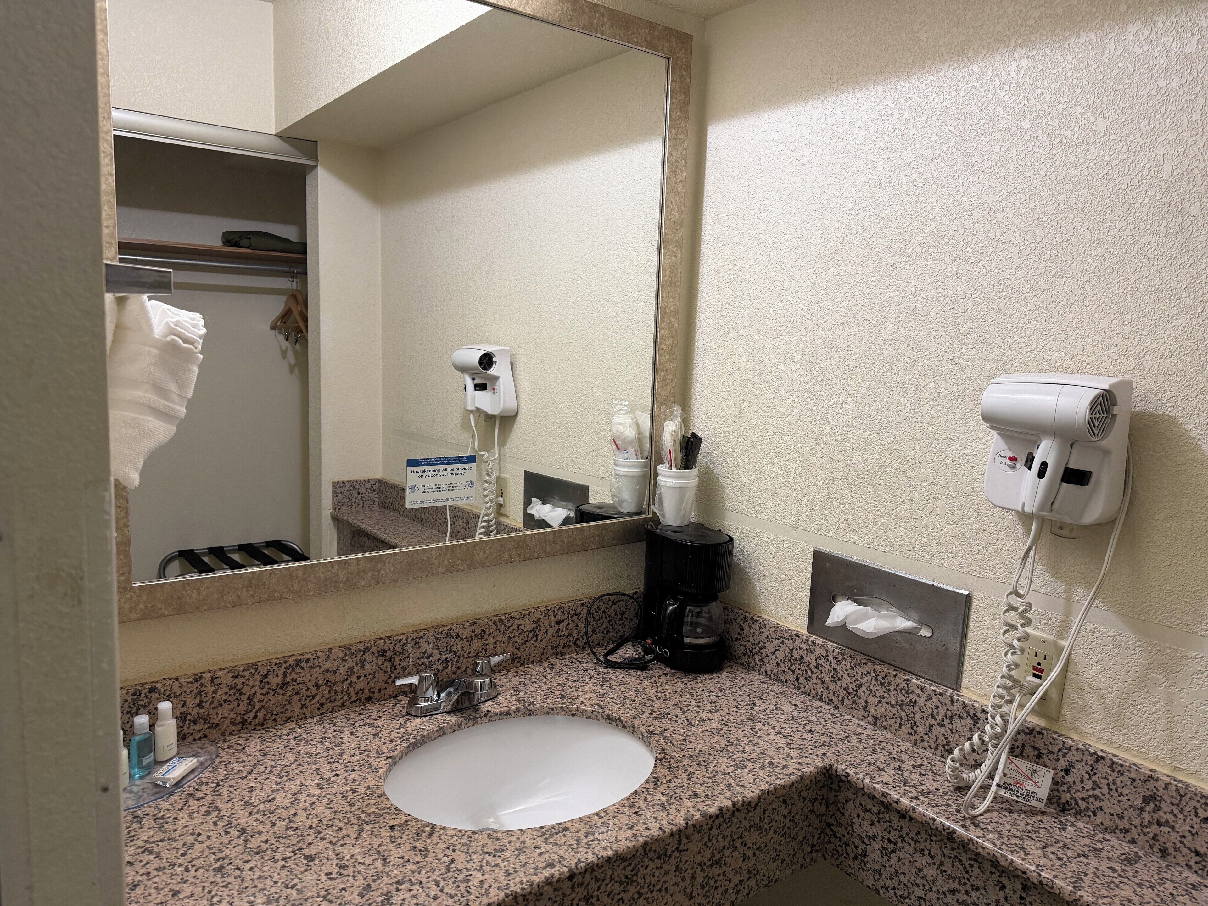 Un baño con encimera de granito, un lavabo, un espejo, un secador de pelo y un perchero para toallas.