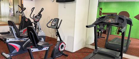 Un gimnasio con cintas de correr, bicicletas estáticas y un televisor en la pared.