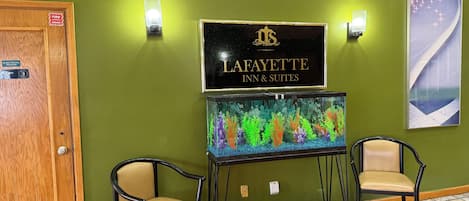 Vastaanottoalue, jossa on Lafayette Inn & Suites -hotellin kyltti, kaksi tuolia, akvaario ja ovi, jossa lukee ”Sähköhuone”.