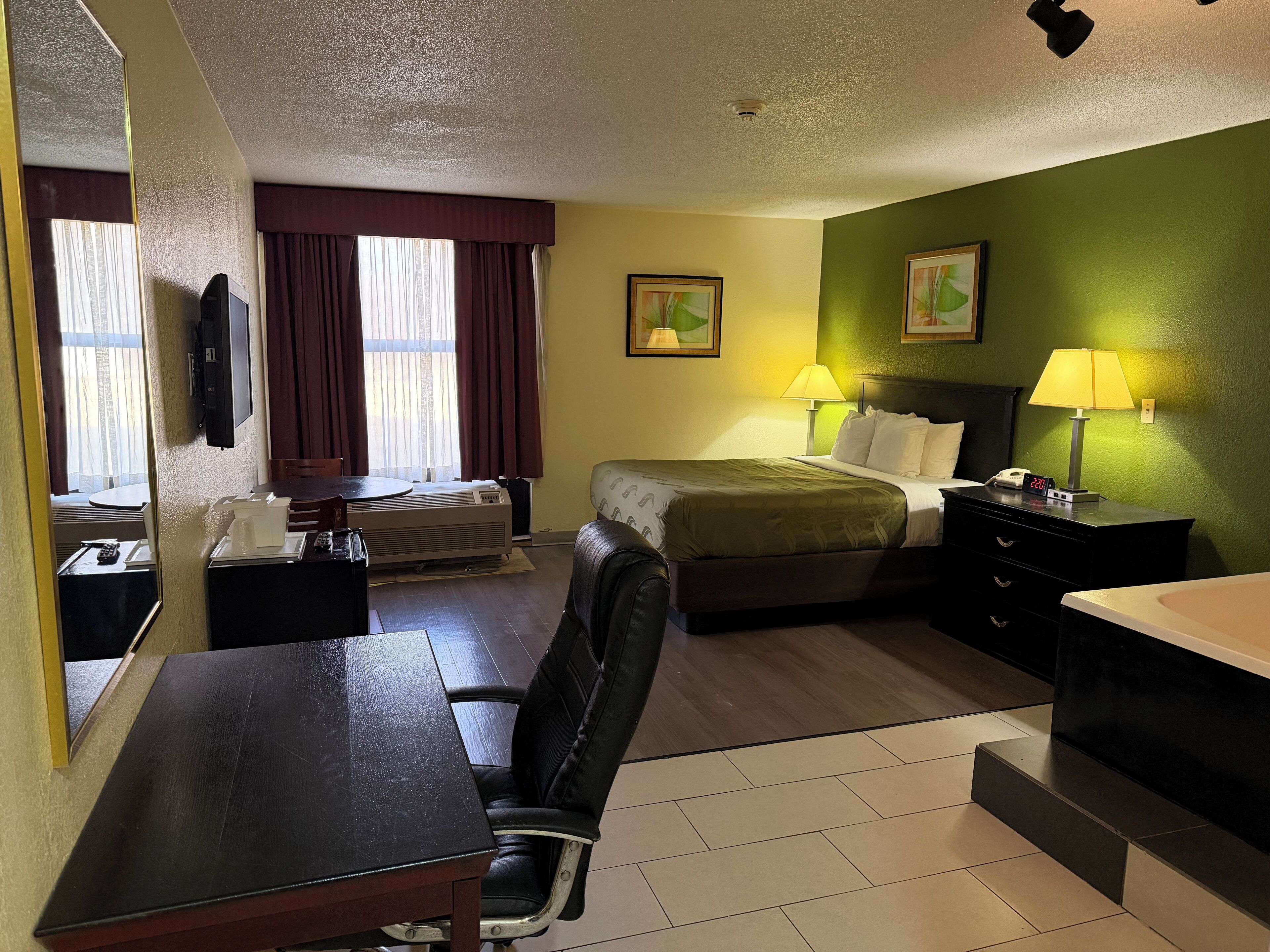 A hotel room with a bed, a desk, a chair, a nightstand, and a lamp.