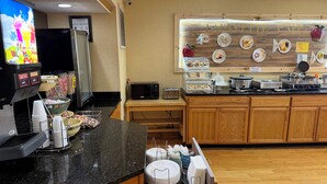 Un coin cuisine équipé d’une machine à café, d’un four à micro-ondes, d’un grille-pain et de divers aliments présentés sur une planche en bois.