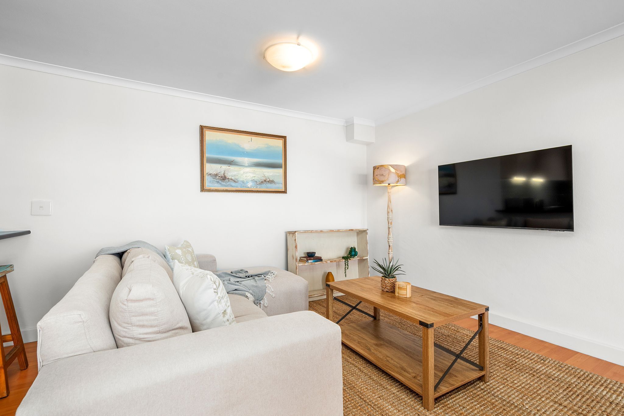 A modern living room with a sofa, a wooden coffee table, a flat-screen TV, a painting, and a lamp.