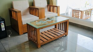 Un conjunto de sofá de madera con una mesa de centro de vidrio en una habitación con piso de baldosas y una ventana con cortinas.