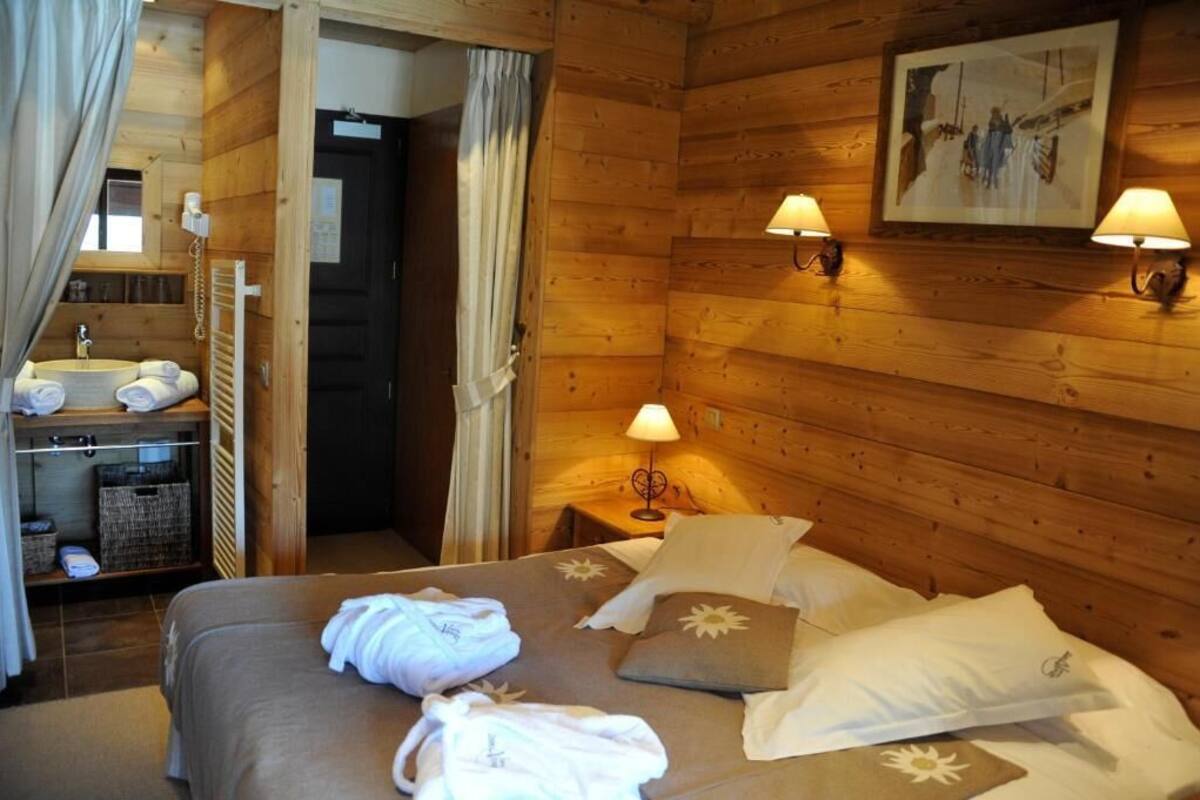 Camera da letto in una baita di legno, con un letto, due lampade da comodino, un quadro appeso al muro e un bagno con lavandino e asciugamani.