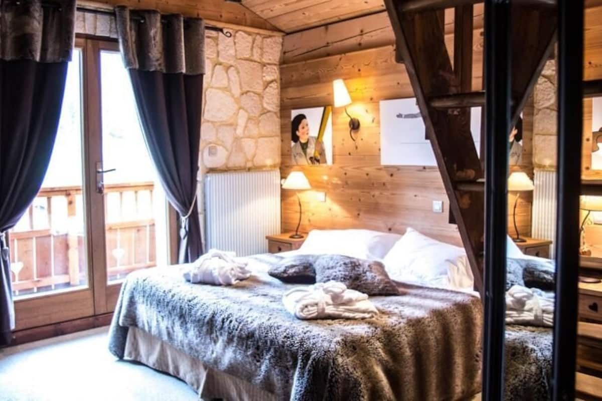 Una stanza accogliente con un letto, soffitto in legno, pareti in pietra e una finestra con tende.