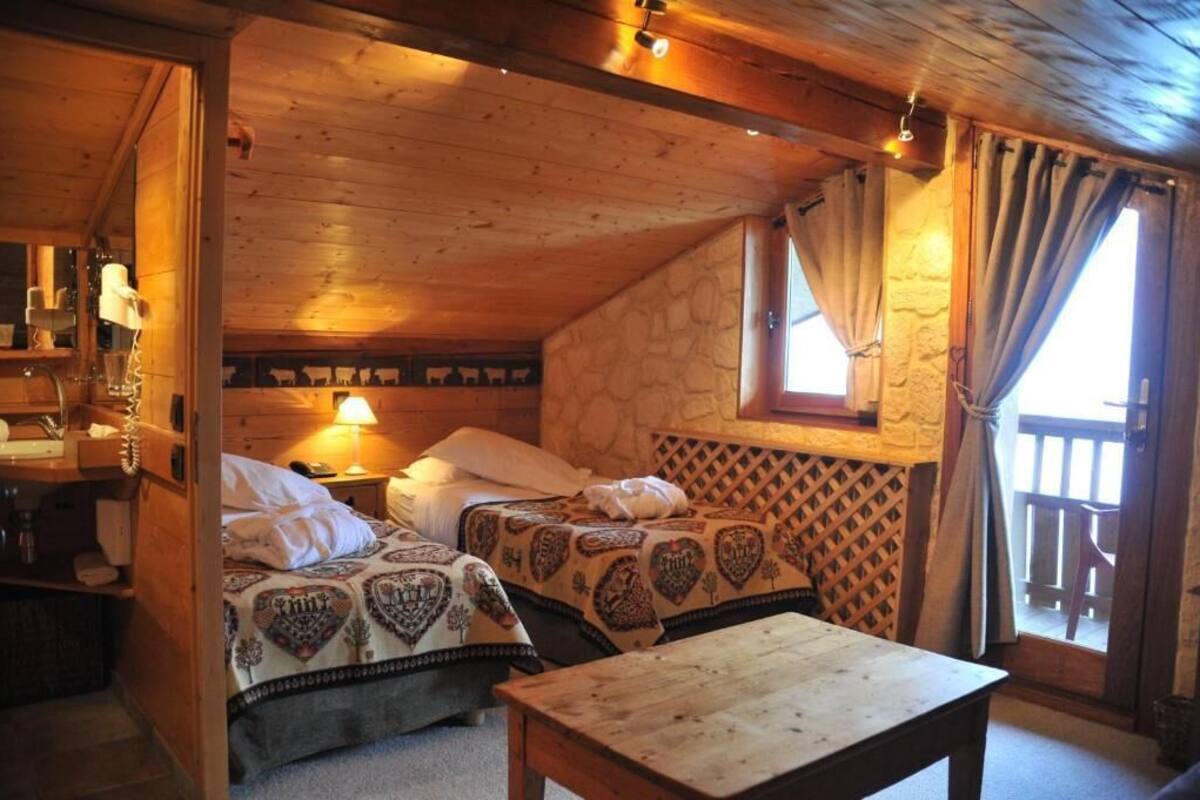 Una stanza accogliente in stile chalet con due letti, un tavolo di legno e un muro in pietra.