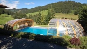 A pool area with a glass-enclosed structure, surrounded by greenery and hills.