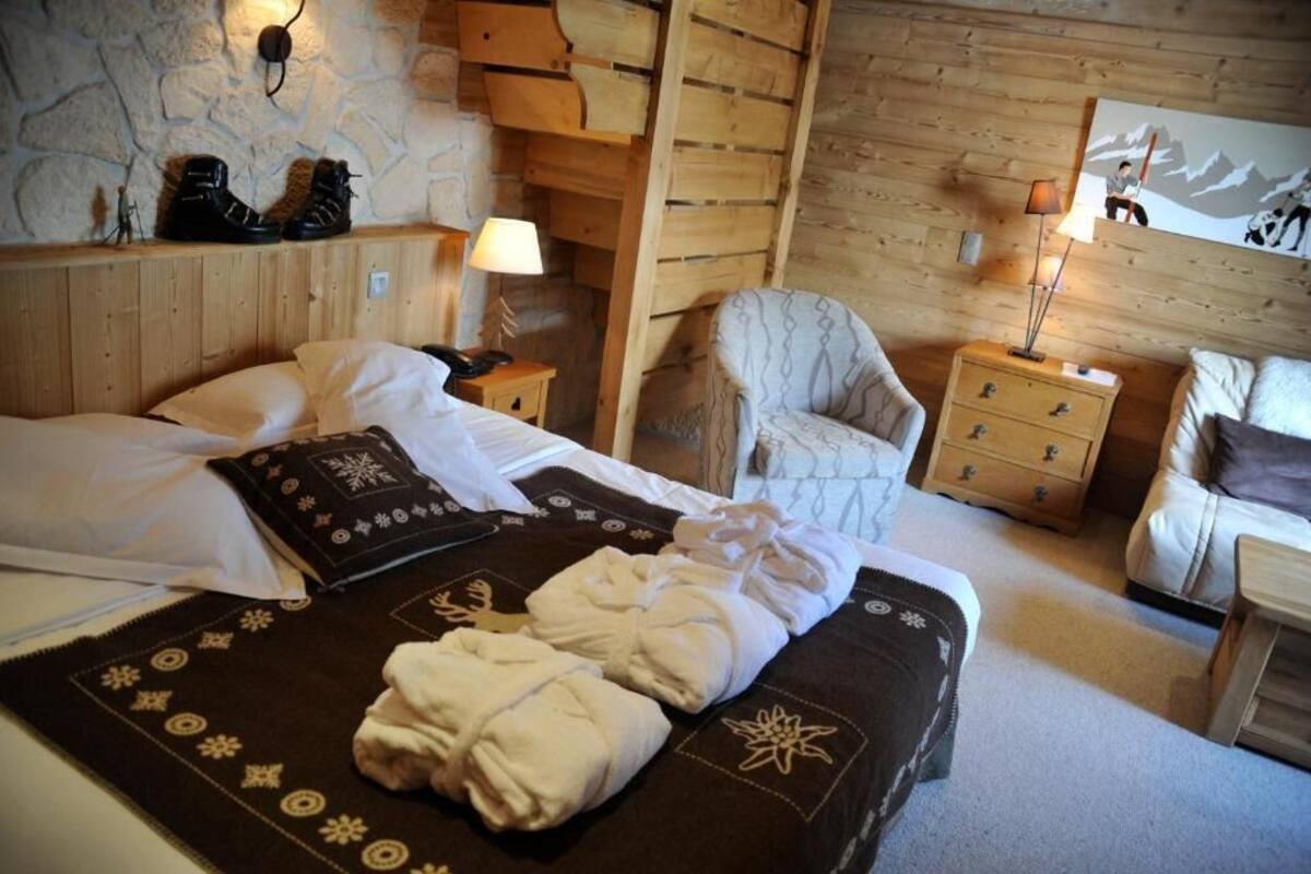 Una camera d'albergo accogliente con un letto, una sedia, un comodino e una lampada a parete.