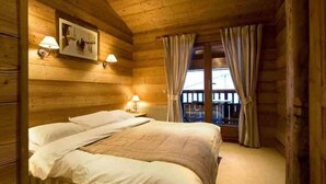 A wooden cabin bedroom with a bed, two bedside lamps, a picture on the wall, and a window with curtains.