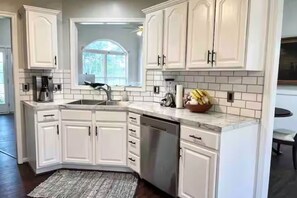 A kitchen with white cabinets, a built-in dishwasher, and a window with a view of greenery. - Very Convenient & Modern with Beautiful view (Country Club)