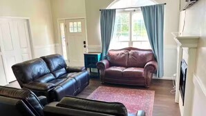 A living room with a brown leather sofa, a red leather armchair, and a blue curtain. - Very Convenient & Modern with Beautiful view (Country Club)
