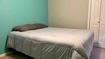 Un lit simple avec une couvre-lit grise dans une pièce aux murs de couleur turquoise et à la porte blanche.